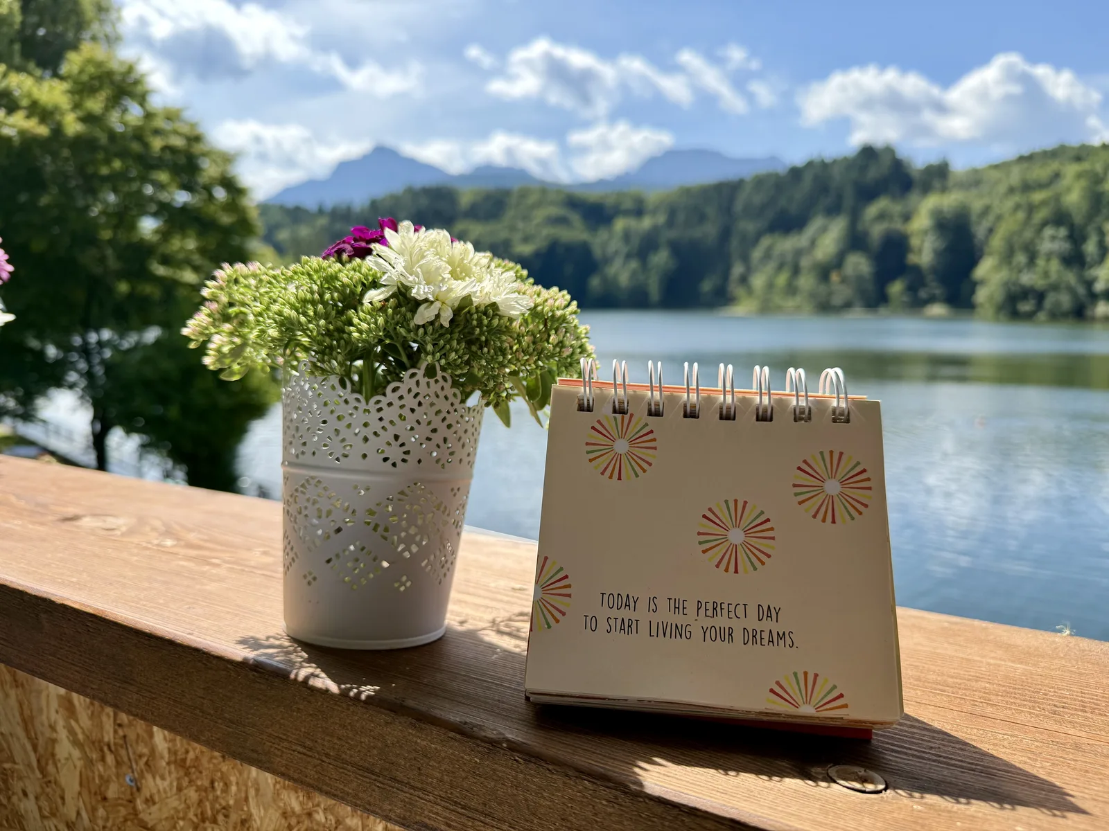 Blumenstrauss und Zitat-Kalender auf einem Gelaender am See